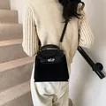 Detalle de bolso trapezoidal negro con cierre giratorio plateado y texturas contrastadas - Negro