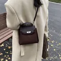 Detalle del bolso Kelly de gamuza marrón oscuro con cierre metálico y fondo otoñal - Marrón