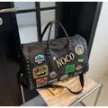 Detail view of large black travel bag with embroidered badges and silver square metal studs - Black