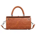 Detail of floral embossed texture and silver hardware on a brown rectangular handbag - Brown