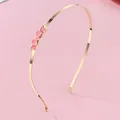 Détail d'un serre-tête fin en métal doré avec un délicat papillon en émail rose décoratif - Forme de nœud papillon