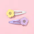 Détail de pinces à cheveux fleurs évidées jaunes et violettes sur un fond rose tendre - Barrettes à Cheveux Fleurs Violettes Et Jaunes