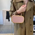 Sac à main ovale rose avec cadre doré et bandoulière chaîne porté par un modèle - Rose Lotus