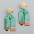 Macro detail of pencil-shaped clay earrings with hammered gold metal discs and pink erasers - Cyan