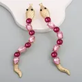 Elegant gold snake earrings with pink crystals on a white wavy display stand - Pink
