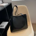Bolso tote grande de cuero negro con correa ancha y remaches sobre una silla beige - Negro