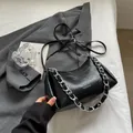 Bolso negro fruncido con cadena plateada y logo sobre una chaqueta gris moderna - Negro