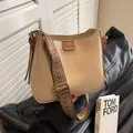 Bolso tipo cubo beige con correa tejida étnica sobre un sofá de cuero negro - Caqui