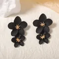 Detail of matte black floral earrings with golden centers on textured background - Black