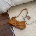 Brown leather underarm bag with metal buckle straps and animal charm on plush rug - Dark Brown