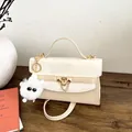 Sac kelly crème élégant avec ferrures dorées et breloque en peluche sur table en bois - Avec Pendentif / Blanc