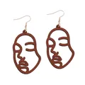 Macro view of laser cut hollow wooden face earrings with smooth brown artistic texture - Brown