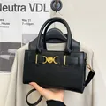 Elegant black leather handbag with gold heart buckle shown in a lifestyle setting - Black