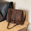 Vintage brown messenger bag with matte texture and buckle strap on stone base - Coffee