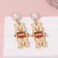 Golden MOM earrings with football motif and white faux pearls on elegant pink display - Milky White