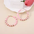Detail of pink clay bead hoop earrings with gold metal accents on a decorative background - Pink
