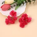 Detail von roten Stoffblumen-Ohrringen mit Metallketten und Perlen vor warmem Hintergrund - Fuchsia