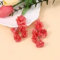Detail von roten Chiffonblumen-Ohrringen auf einem dekorativen weißen Tablett - Rosenrosa