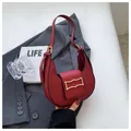 Sac croissant bordeaux chic avec boucle dorée posé sur un costume gris élégant - Rouge