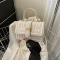 Weiße gesteppte Handtasche mit Goldverschluss auf weißem Blazer im Metallkorb - Weiß