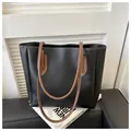 Detalle de bolso tote negro minimalista con correas marrones y costuras blancas en contraste - Negro