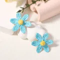 Vista macro dettagliata degli orecchini a margherita in rafia azzurra intrecciata a mano - Orecchini Blu