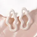 Dettaglio degli orecchini a onde irregolari con finitura crema perlata e cangiante - Bianco latte