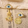 Vintage vergoldete asymmetrische Evil Eye Ohrringe mit Sonnen- und Münzanhängern auf Papier - Blauer böser Blick