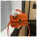 Detail der orangefarbenen Tasche mit Krokoprägung, Goldverschluss und Plüschanhänger - Orange