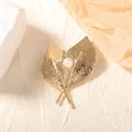Detailed close-up of golden leaf brooch with hammered texture and a white center pearl - Gold