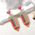 Creative beaded pencil earrings with a pink heart stud shown on a stone display - Colorful