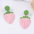 Detail van handgeweven aardbeien oorbellen met groene bladeren en roze raffia textuur - Aardbeivorm / Aardbei Roze