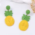 Handgemaakte raffia ananas oorbellen met felgeel geweven fruit en groene bladeren als accent - Ananasgeel