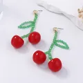 Close-up of handmade beaded cherry earrings with red globes and green leaf beads - Red