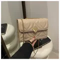 Beige quilted shoulder bag with heart pattern and golden chain strap in a lifestyle shot - Khaki