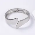 Polished silver alloy open bangle with overlapping wing design on neutral stone background - Small Wing Spring Bracelet / Silver