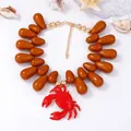 Dettaglio del ciondolo a granchio smaltato rosso e perle marroni su collana a tema marino - Cammello