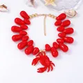Dettaglio ravvicinato di perle rosse a goccia e ciondolo a granchio su collana dorata - Rosso