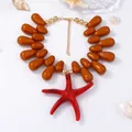 Detailed shot of large red starfish pendant with brown teardrop beads on white background - Tan