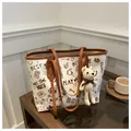 Dettaglio della borsa tote graffiti con ciondolo a orso su tavolo in legno scuro - Con Ciondolo / Marrone Scuro