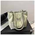 Dettaglio di una borsa tote verde chiaro plissettata con un decoro a farfalla in metallo - Verde