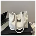Dettaglio della borsa tote in morbida pelle sintetica con farfalla in metallo sulla scrivania - Bianco