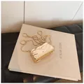 Goldene Clutch aus Metall mit Wellentextur und feiner Kette auf einem Buch - Wellenförmig Rechteckig Gold (Stil 2 Gold)