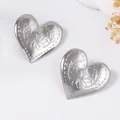 Detalle de pendientes de corazón plateados con motivos florales en relieve y borde texturizado - Plateado