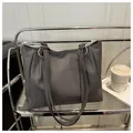 Detail of dark grey textured tote bag featuring silver metal rings and long shoulder straps - Black