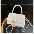 Minimalist white leather handbag with elegant gold buckle on a black studio background - White