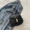 Classic black leather saddle bag with rectangular gold buckle on denim background - Black