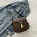 Dark brown saddle crossbody bag with golden lock on denim jacket background - Brown