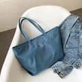Große Nylontasche in Morandi-Blau mit Schultergurt und Logo-Patch auf weißem Stuhl - Blau