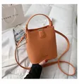 Orange faux leather bucket bag with top handle and strap on white quilted background - Orange